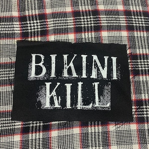 May include: Black fabric patch with white text that reads "Bikini Kill".