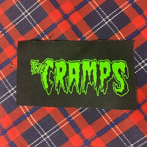 May include: A black fabric patch with the words "The Cramps" in green dripping letters.