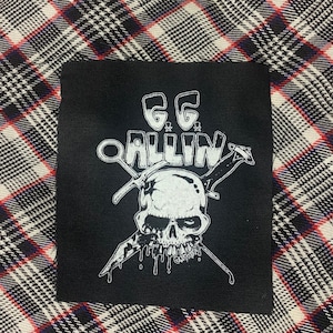 May include: Black and white patch with a skull and crossbones design. The text "GG ALLIN" is written above the skull.