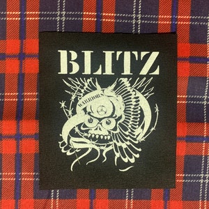 May include: Black and white embroidered patch with the word "BLITZ" in white lettering and a skull with wings and barbed wire. The skull has the word "WARRIORS" above it.