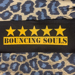 May include: A black fabric patch with five gold stars and the text "BOUNCING SOULS" in gold letters.