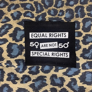 May include: A black patch with white text that reads "EQUAL RIGHTS 50♀ ARE NOT 50♂ SPECIAL RIGHTS" on a brown and blue leopard print background.