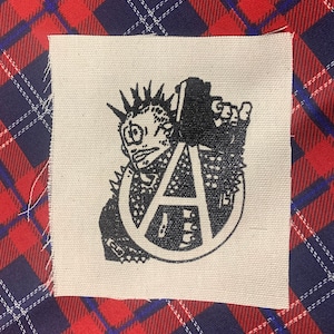 May include: Black and white iron-on patch featuring a punk rock character with a mohawk holding a microphone and an anarchy symbol.