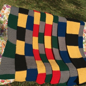 May include: Seven crocheted scarves in different colors, including yellow, green, red, blue, and gray. The scarves are arranged in a row on a floral patterned surface.