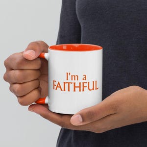 Puede incluir: Taza de cerámica blanca con borde y asa naranja. La taza tiene el texto "I'm a FAITHFUL" impreso en naranja.