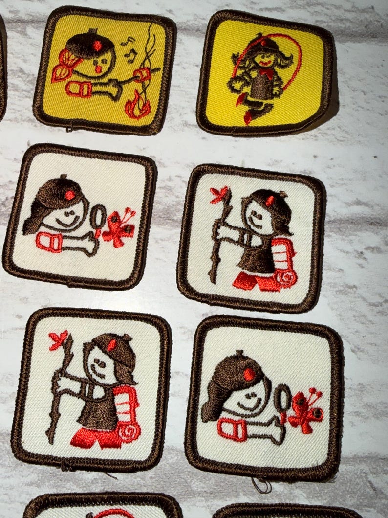 May include: A selection of embroidered patches, each showcasing a cartoon figure in outdoor pursuits. The patches have either a white or yellow backdrop, framed by brown borders. The character, wearing a brown hat and red details, is shown engaged in activities such as playing music, skipping, and hiking.