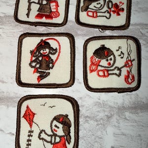 May include: A set of embroidered patches with a cartoon character in different poses. Each square patch has a cream background and a brown border. The character, wearing a brown hat and outfit with red details, is shown doing activities such as playing a musical instrument and skipping.