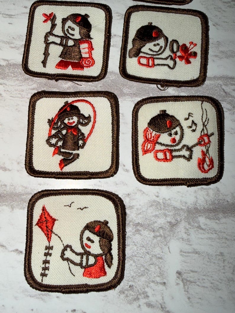May include: A set of embroidered patches with a cartoon character in different poses. Each square patch has a cream background and a brown border. The character, wearing a brown hat and outfit with red details, is shown doing activities such as playing a musical instrument and skipping.
