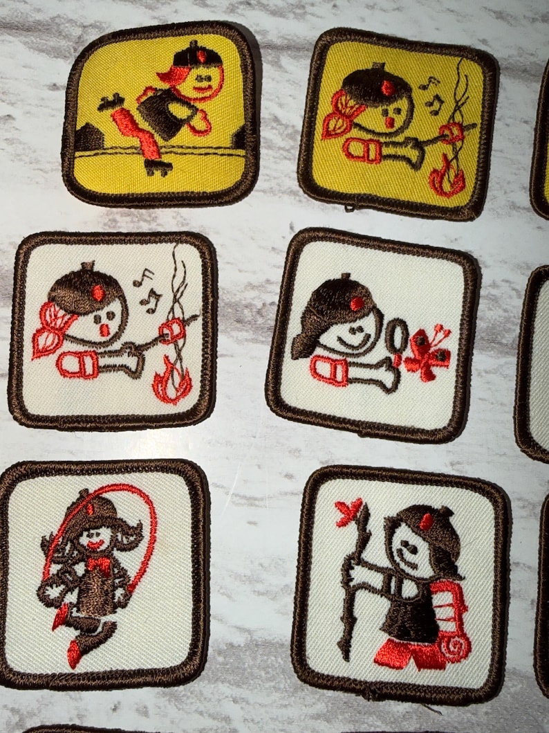 May include: A selection of embroidered patches with cartoon figures engaged in different activities. The patches are square with a brown border. The figures are in brown, red, and black, set against yellow or white backgrounds.