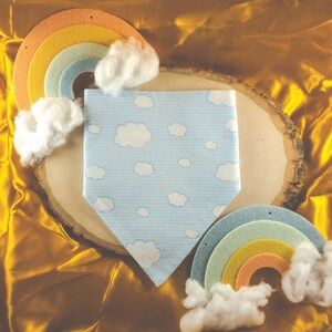 May include: A blue bandana with a white cloud pattern, a rainbow with yellow, orange, and green stripes, and a white fluffy cloud. The bandana is on a wooden surface.