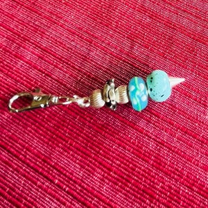 May include: A silver key chain with a blue and white glass bead charm. The charm has a pointed end and is decorated with small white dots.