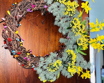May include: A brown twig wreath decorated with colorful beads and accented with sprigs of yellow flowers and green foliage.