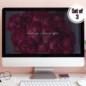 May include: A computer screen displaying a close-up image of a bouquet of deep red peonies with the text "darling, i fancy you." The screen is on a white desk with a coffee mug, glasses, a phone, a keyboard, and a mouse.