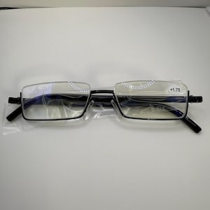 May include: Black rimmed reading glasses with a +1.75 magnification. The glasses have a rectangular shape with a half-rim design. The lenses are clear, and the glasses are in a clear plastic sleeve.