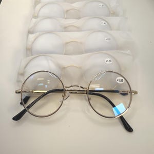 May include: Round eyeglasses with gold frames and black temples. Several pairs of reading glasses are visible, each with a +1.50 strength label. The glasses are packaged in white protective sleeves.