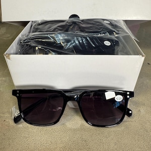 May include: Black square-framed sunglasses with dark lenses are displayed in front of a white box. The sunglasses have a +2.25 strength label. Several pairs of sunglasses are visible inside the box.