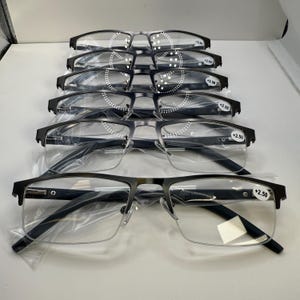 May include: A stack of black metal-framed reading glasses with clear lenses. Each pair is marked with a +2.50 strength indicator. The glasses have a half-rim design and are individually wrapped in clear plastic.