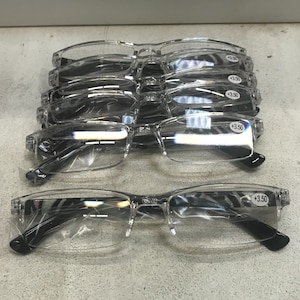 May include: A stack of five clear plastic reading glasses with black frames. Each pair has a label that reads " +3.50".