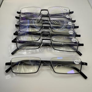 May include: A stack of black-framed reading glasses with clear lenses. Each pair is marked with a +1.75 magnification. The glasses have a rectangular shape with a semi-rimless design. The frames are black and the lenses are clear.