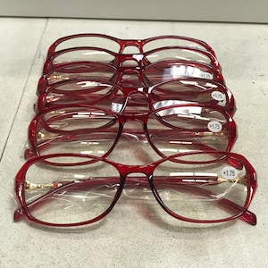 May include: Five pairs of red reading glasses with a +1.75 magnification. The glasses have a rounded, oval shape.