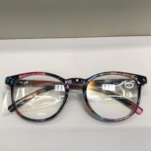 May include: A pair of blue, pink, and brown reading glasses with a +4.00 diopter strength. The glasses have a round frame and clear lenses.