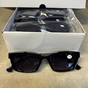 May include: A box of black reading glasses with a +2.25 magnification. The glasses have a rectangular frame and are packaged in individual plastic sleeves. The box is white and contains multiple pairs of glasses.