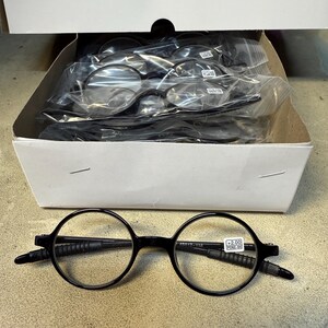 May include: Black round-frame reading glasses with +2.00 magnification are displayed in front of a box containing multiple pairs. The glasses have a classic design with a black frame and clear lenses. The box is white and contains several pairs of glasses in individual plastic bags.