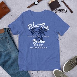 May include: A blue t-shirt with a white graphic design that says "West Bay" with palm trees and the text "relax & enjoy Roatan Honduras Island Palm Co."