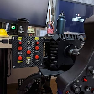 Op de afbeelding: Een zwart race stuur en pedaalset met een carbonfiber ontwerp. Het stuur heeft een zwarte basis met een zilveren Fanatec logo. De pedalen hebben een zwarte basis met rode knoppen en een zwart-wit carbonfiber ontwerp. De set is aangesloten op een computermonitor en een zwart bedieningspaneel met rode knoppen en een carbonfiber ontwerp.