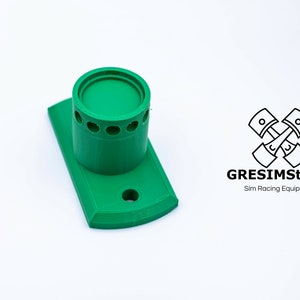 May include: Green 3D printed wall mount with a round opening and a series of small holes around the opening. The mount is designed to hold a racing simulator accessory. GRESIMStudio Sim Racing Equipment.