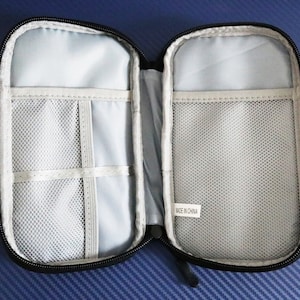 May include: Black zippered pouch with a gray mesh interior. The pouch has multiple compartments and a zipper closure. The pouch has a label that reads "Made in China".