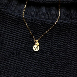 May include: A gold chain necklace with a small round pendant featuring the letter "W" and a tiny star charm.