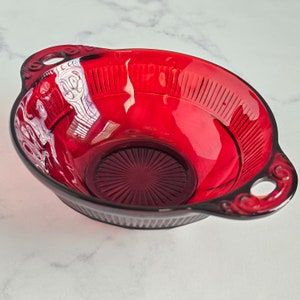May include: A red glass bowl with a decorative design and two handles. The bowl is made of ruby red glass and has a deep, round shape.