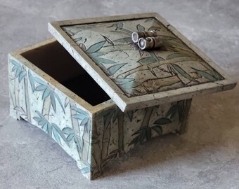 May include: A ceramic box with a lid, decorated with a bamboo design in shades of green, brown, and white. The lid has a decorative knob in the shape of two scrolls.