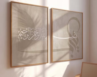 May include: Two framed prints with beige backgrounds and white Arabic calligraphy. The left print features the phrase "Allah is the Most Merciful" and the right print features the phrase "Bismillah", which means "In the name of Allah".