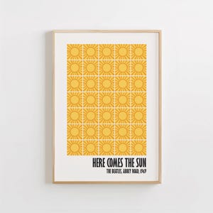 Peut inclure: Impression d'art encadr&eacute;e avec un motif r&eacute;p&eacute;t&eacute; de soleils jaunes sur fond blanc. Le texte "HERE COMES THE SUN" est imprim&eacute; en noir, avec "THE BEATLES, ABBEY ROAD, 1969". L'impression est dans un cadre en bois brun clair.