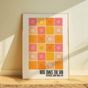 Peut inclure: Impression d'art encadr&eacute;e avec une grille de soleils color&eacute;s dans des tons de rose, orange et jaune. Le texte "HERE COMES THE SUN" et "THE BEATLES, ABBEY ROAD, 1969" est imprim&eacute; en bas. L'&oelig;uvre est pr&eacute;sent&eacute;e dans un cadre dor&eacute;.