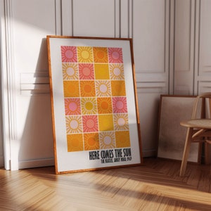 Peut inclure: Une affiche encadr&eacute;e avec une grille d'illustrations de soleil dans des tons de rose, jaune et orange. Le texte "HERE COMES THE SUN" et "THE BEATLES, ABBEY ROAD, 1969" est imprim&eacute; en dessous. Le cadre est marron chaud.