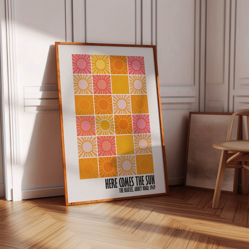 Peut inclure: Une affiche encadr&eacute;e avec une grille d'illustrations de soleil dans des tons de rose, jaune et orange. Le texte "HERE COMES THE SUN" et "THE BEATLES, ABBEY ROAD, 1969" est imprim&eacute; en dessous. Le cadre est marron chaud.