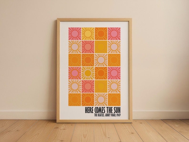Peut inclure: Impression d'art encadr&eacute;e avec une grille d'illustrations de soleil dans des tons de rose, jaune et orange. Le texte "HERE COMES THE SUN" est affich&eacute; en dessous de la grille, avec "THE BEATLES, ABBEY ROAD, 1969" en dessous.