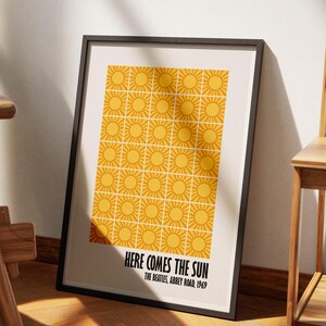 Peut inclure: Impression d'art encadr&eacute;e avec un motif r&eacute;p&eacute;t&eacute; de soleils jaunes sur fond cr&egrave;me. Le texte "HERE COMES THE SUN" et "THE BEATLES, ABBEY ROAD, 1969" sont imprim&eacute;s en noir en bas. Le cadre est noir.