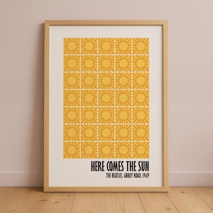 Peut inclure: Impression encadr&eacute;e avec une grille de soleils jaunes sur fond cr&egrave;me. Le texte noir indique "HERE COMES THE SUN" et "THE BEATLES, ABBEY ROAD, 1969". L'&oelig;uvre est pr&eacute;sent&eacute;e dans un cadre en bois brun clair.