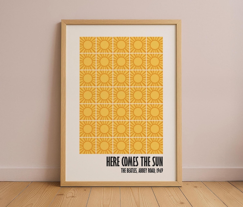 Peut inclure: Impression encadr&eacute;e avec une grille de soleils jaunes sur fond cr&egrave;me. Le texte noir indique "HERE COMES THE SUN" et "THE BEATLES, ABBEY ROAD, 1969". L'&oelig;uvre est pr&eacute;sent&eacute;e dans un cadre en bois brun clair.