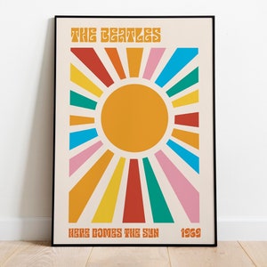 Puede incluir: Un póster de estilo vintage con un sol con rayos de colores, el texto "THE BEATLES" en una fuente retro y las palabras "HERE COMES THE SUN 1969" en la parte inferior.