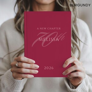 May include: A burgundy hardback book featuring the text A NEW CHAPTER, the name MELISSA, a large script 70th, and the year 2026 printed in a light pink font on the front cover. The word BURGUNDY is printed in the top right corner of the image.