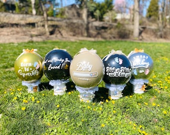 May include: Five black, gold, and silver balloon ornaments with white text and baby footprints. The balloons are on white stands with lace trim. The text on the balloons reads "Born to Sparkle", "What will Baby Be? Loved!", "Baby Loading...", "Pink or Blue we'll love you", and "Sweet Baby".