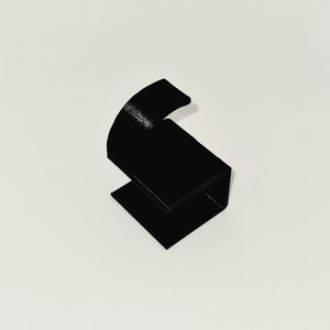 May include: A black, angular, 3D-printed object with a curved top and a rectangular base. The object is a solid black color and appears to be made of plastic. The design is minimalist and modern, suitable for display or functional use.