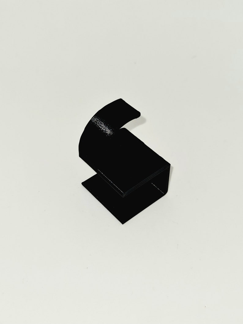 May include: A black, angular, 3D-printed object with a curved top and a rectangular base. The object is a solid black color and appears to be made of plastic. The design is minimalist and modern, suitable for display or functional use.