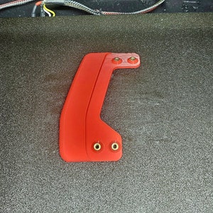 Puede incluir: Una pieza de plástico roja impresa en 3D con cuatro tornillos dorados. La pieza tiene una forma curva y está diseñada para ser unida a otro objeto.