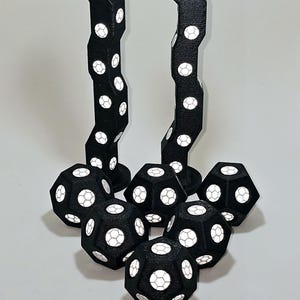 Puede incluir: Un conjunto de dados geométricos negros y blancos con un patrón de panal. Los dados están dispuestos en un grupo con dos pilas de dados verticales.